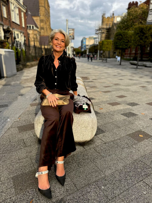 Nikki Garnett seated, wearing the Boden Jewel Button Velvet Shirt in chocolate brown